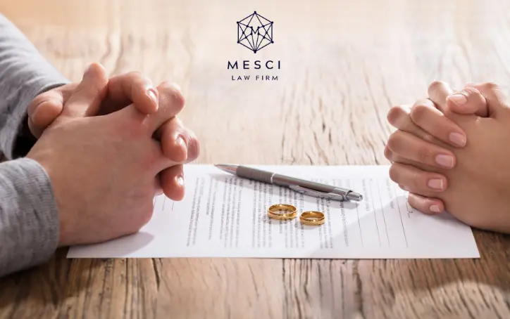 Two individuals placing their hands on a divorce contract, with rings and a pen on the table.